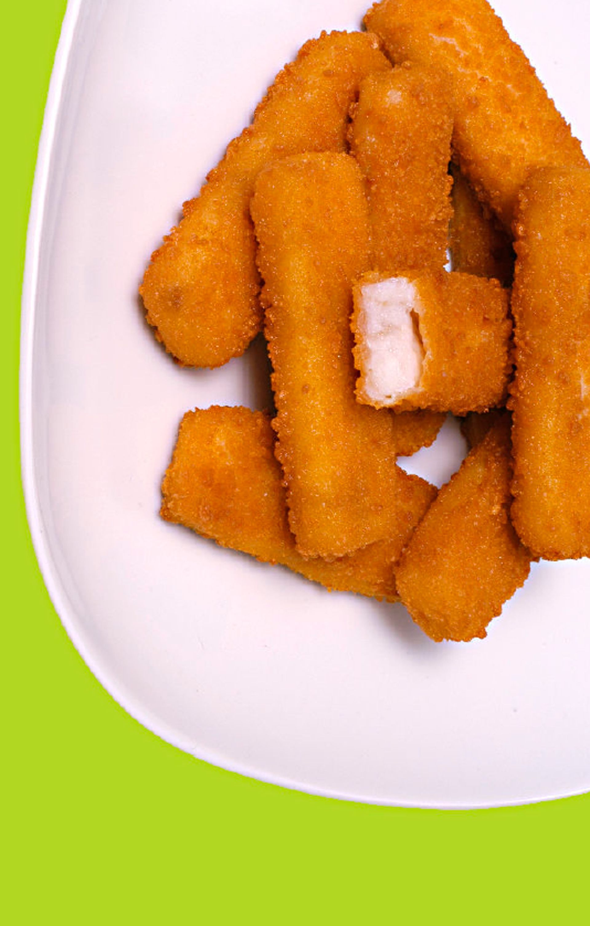 A white plate topped with fried fish sticks on a green background