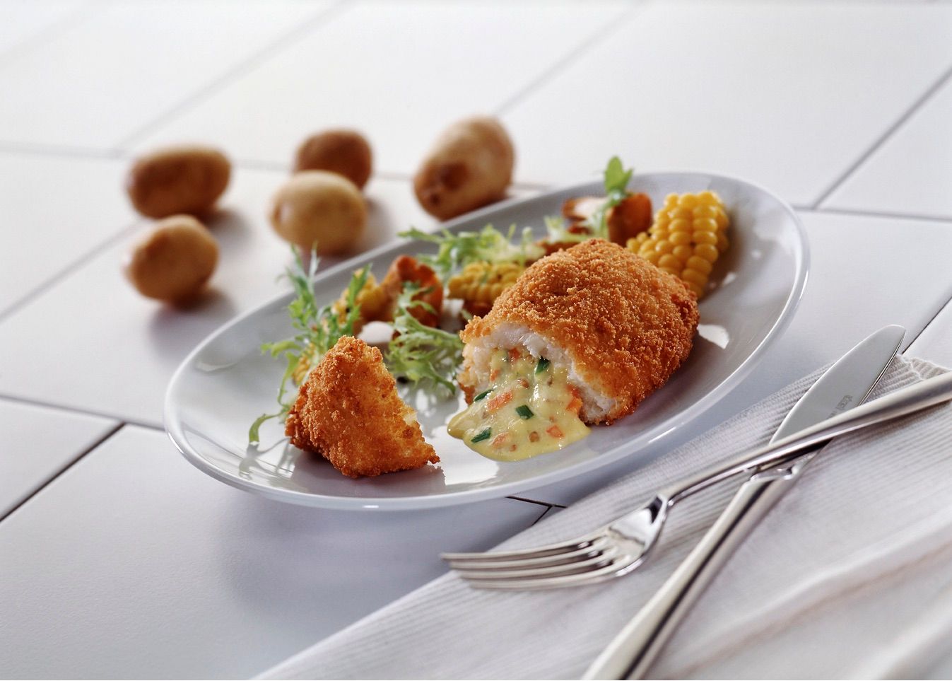 A plate of food with potatoes and corn on the cob on a table.