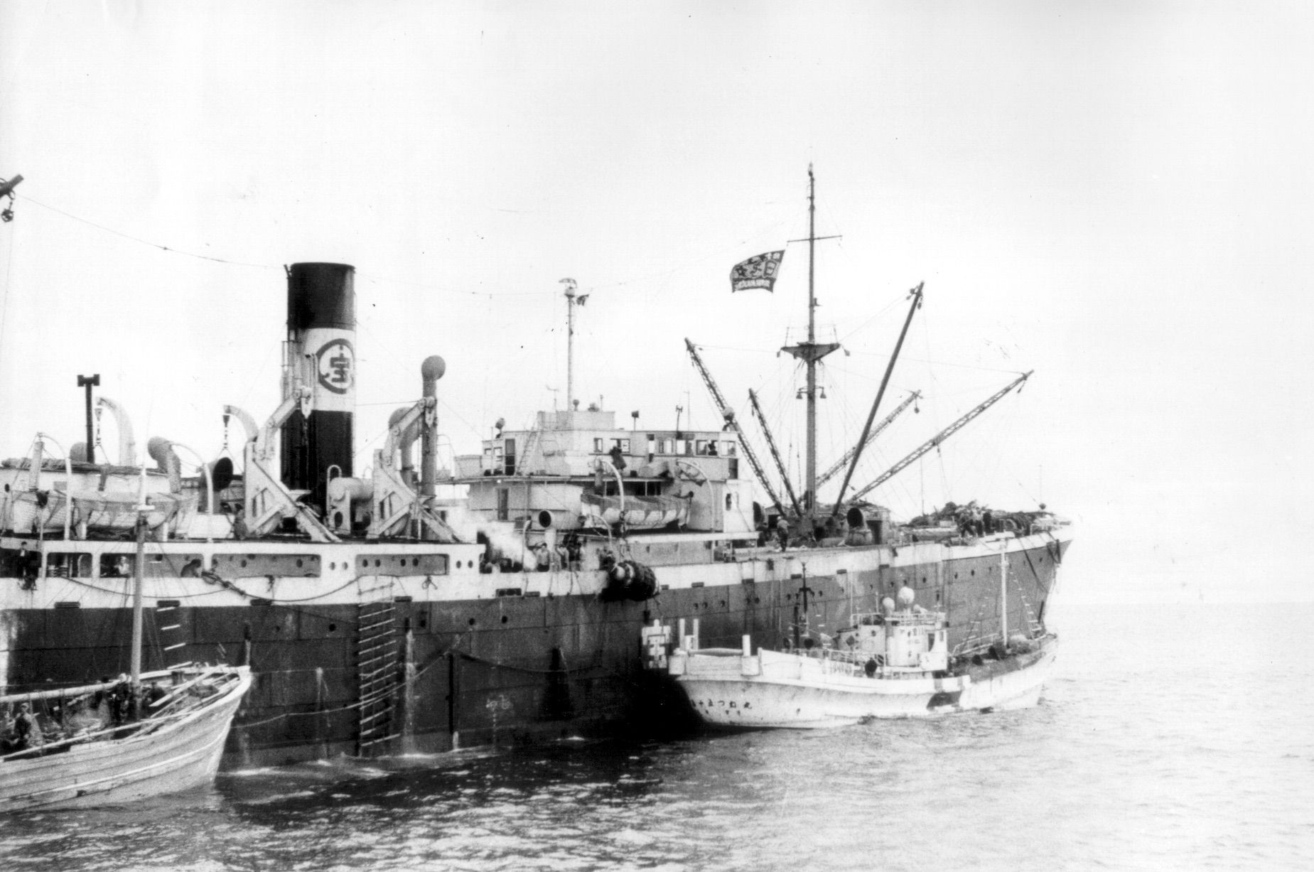 A large ship is docked next to a smaller ship in the water.