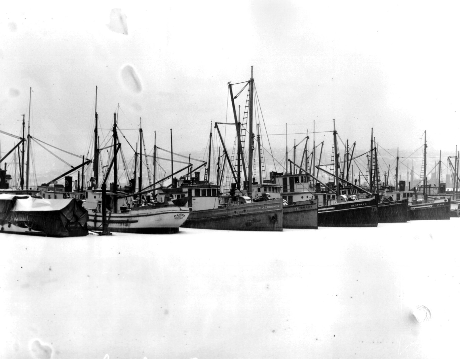 A black and white photo of a row of boats docked in a harbor.