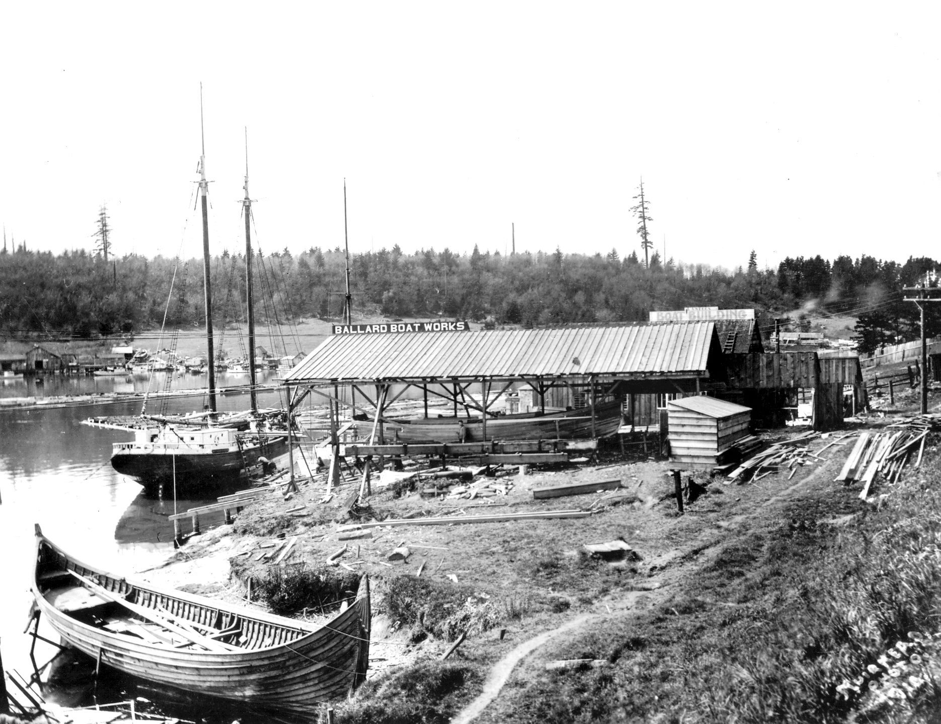 A black and white photo of a boatyard on the shore of a lake.