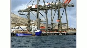 A blue boat is docked in front of a large crane