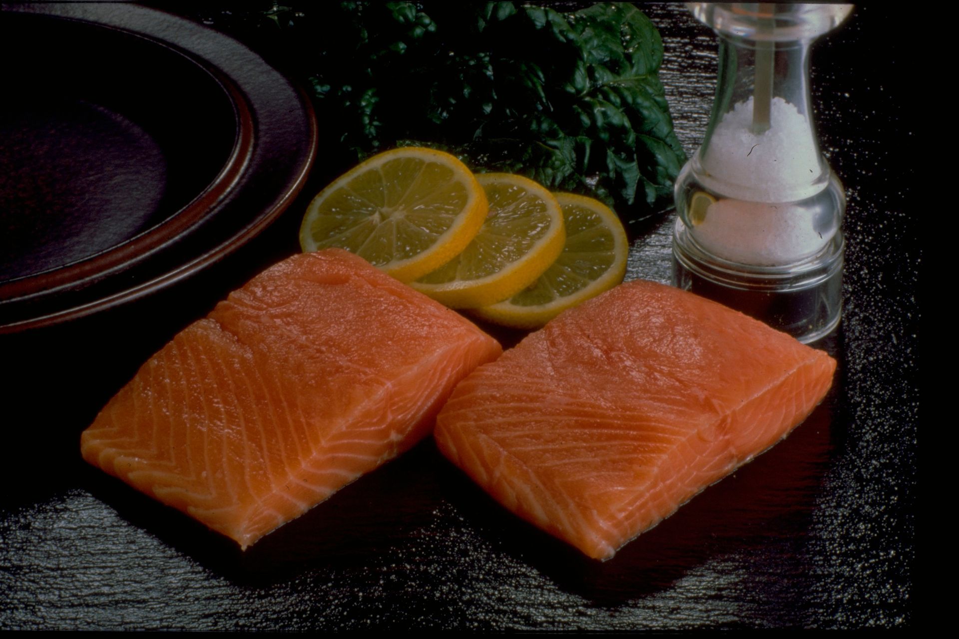 Two pieces of salmon next to lemon slices and a salt shaker