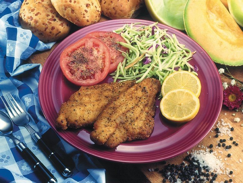 A purple plate topped with fried fish tomatoes and lemon slices