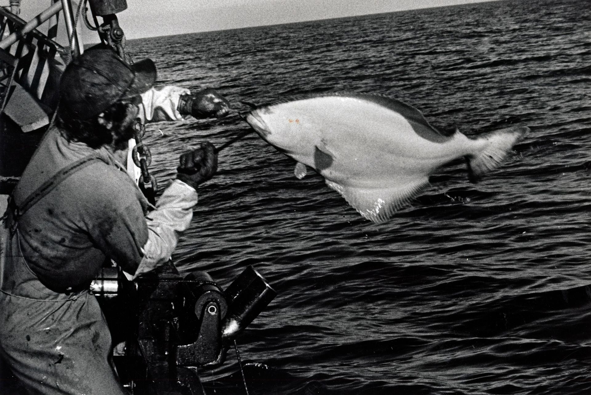 A black and white photo of a man fishing in the ocean