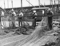 A group of men are working on a fishing net in a black and white photo.