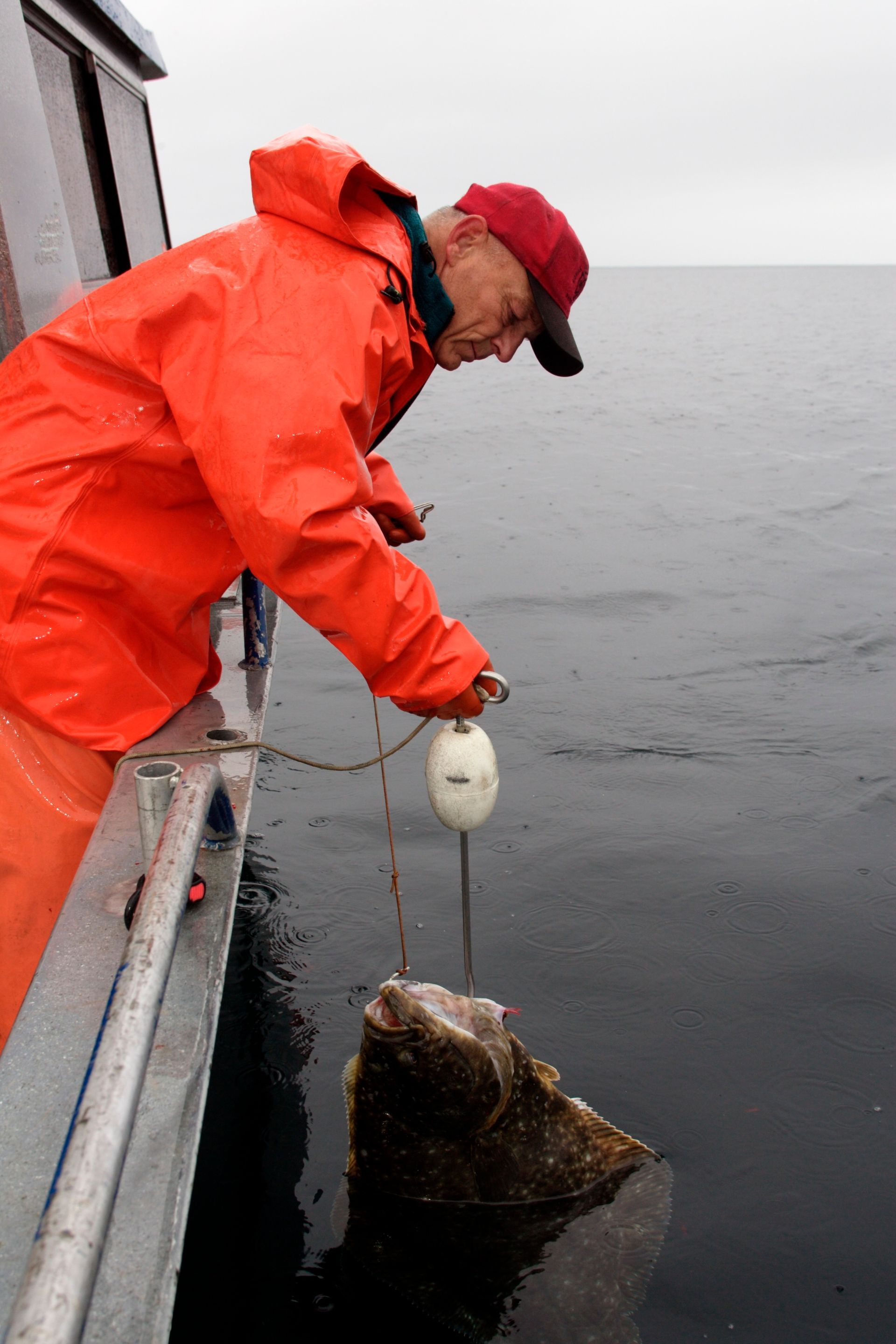 A man in an orange raincoat is fishing in the ocean