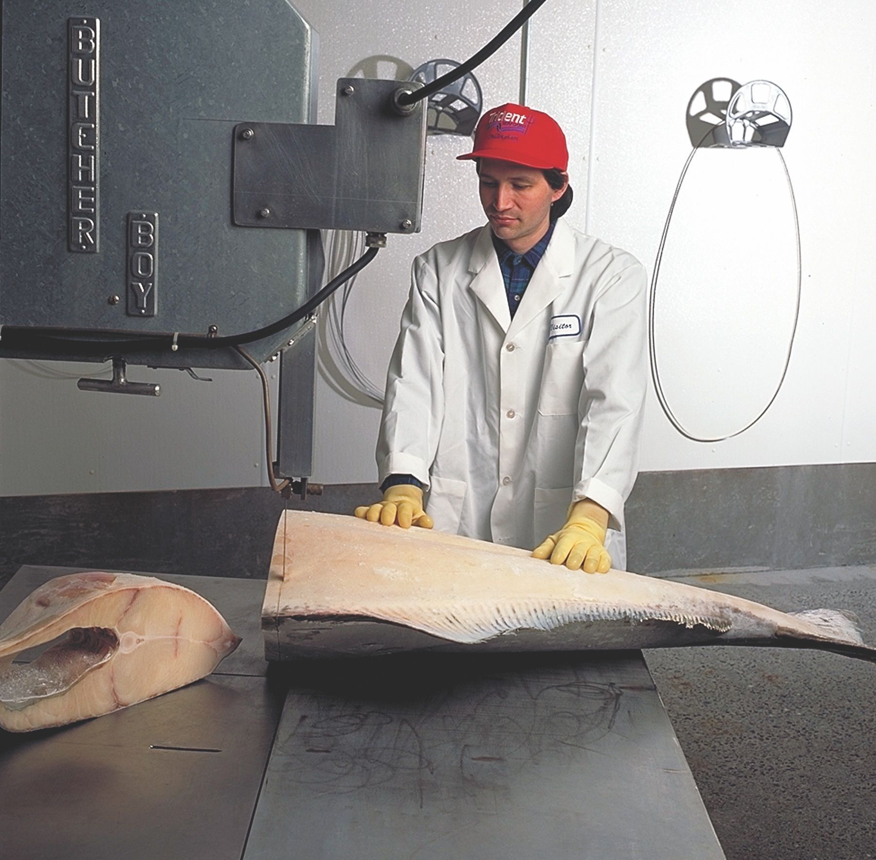 A man in a white coat and red hat is holding a large piece of meat