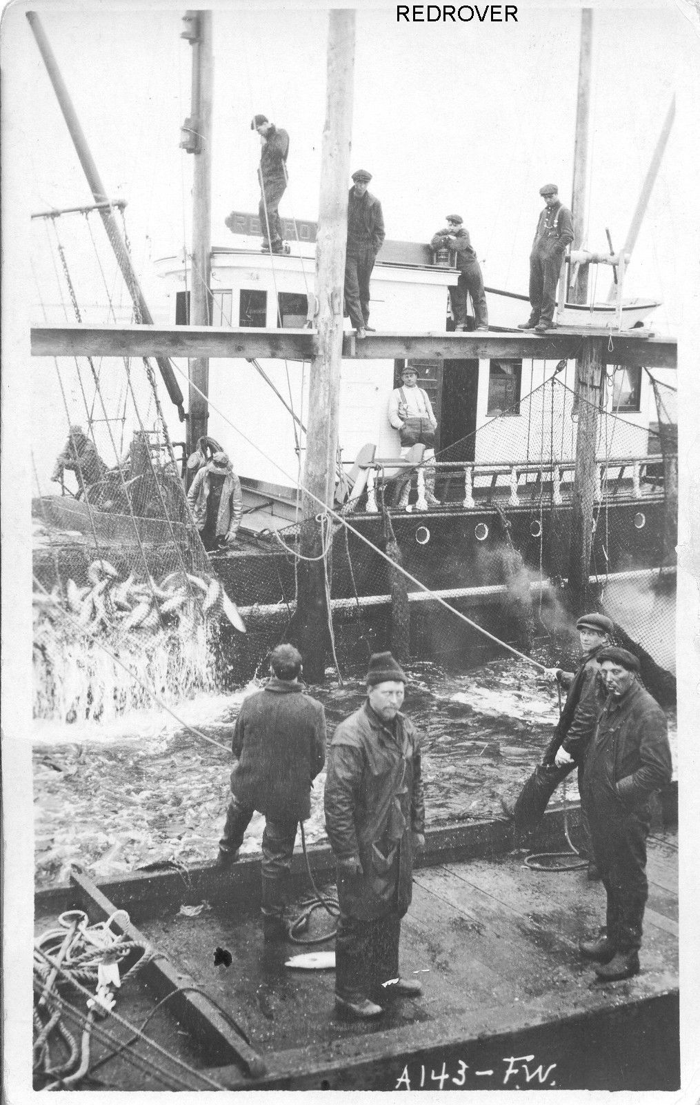A black and white photo of a group of men standing around a boat called redrover