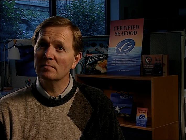 A man is standing in front of a shelf with certified seafood on it.