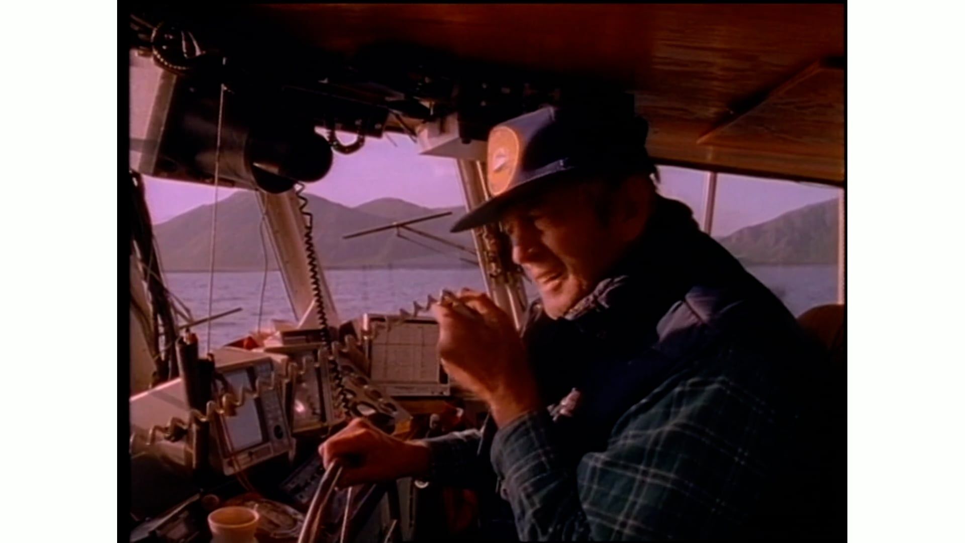 A man is sitting at the steering wheel of a boat.
