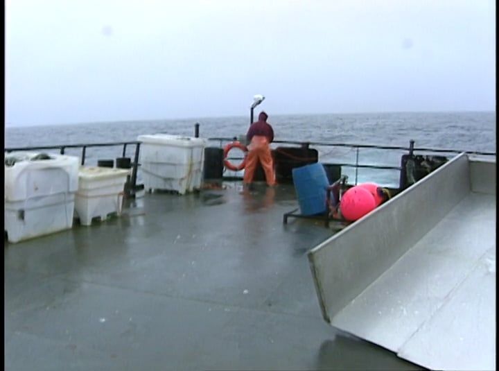 A man is standing on the deck of a boat in the ocean