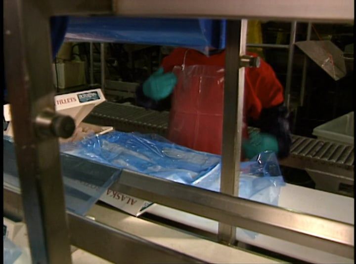 A man in an apron is standing in front of a machine that says alaska on it