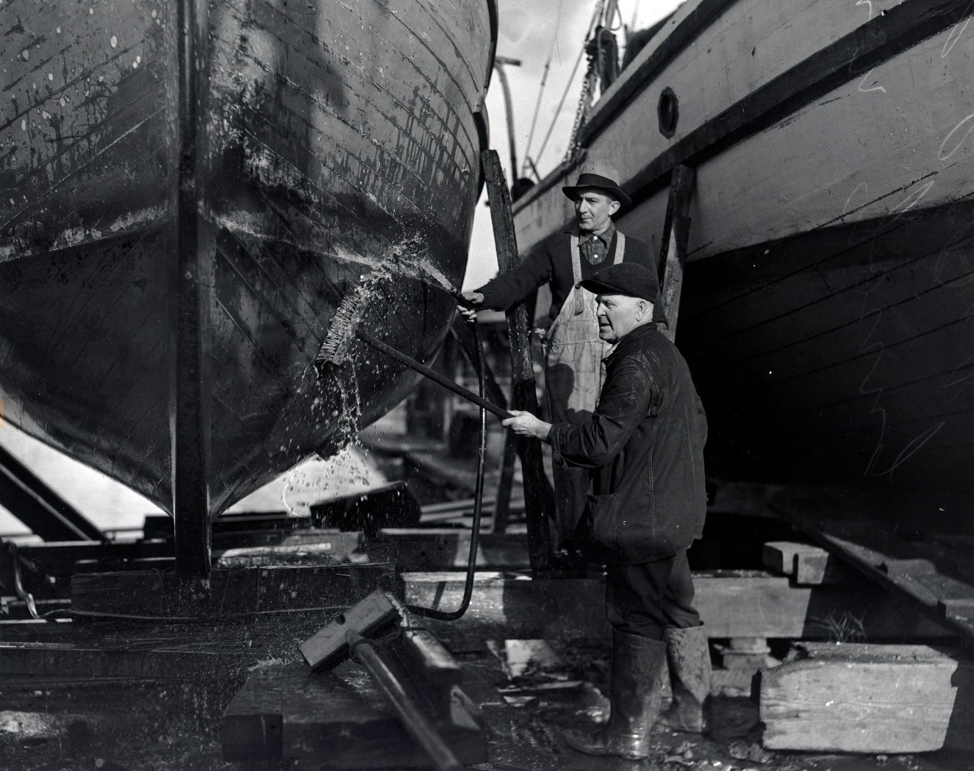 A black and white photo of two men washing a boat