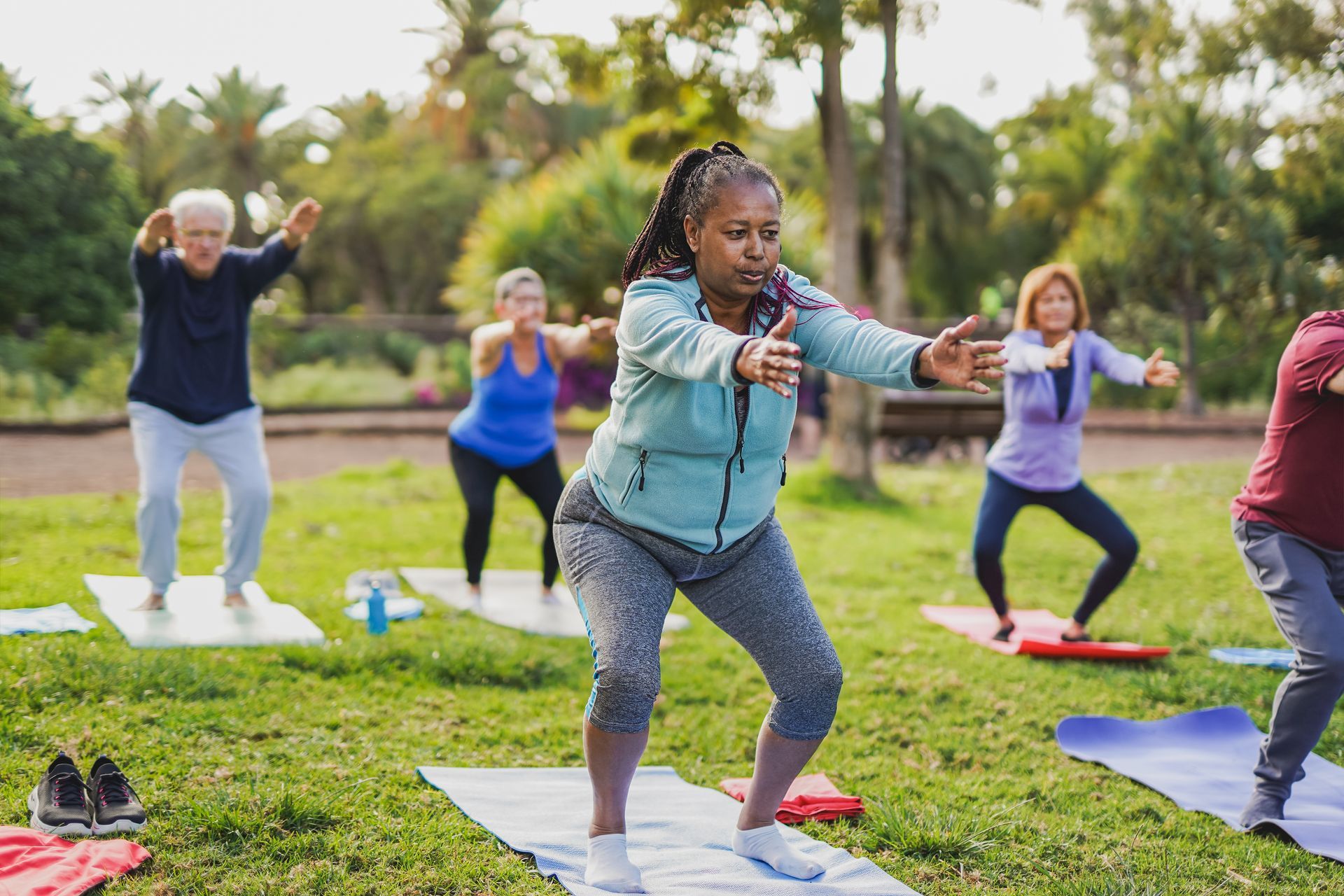 Group of people doing squats outdoors on yoga mats in a park.