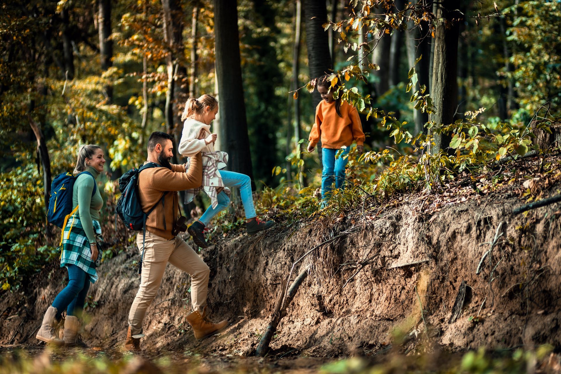 Family hiking in a forest, father lifting child. Autumn trees and trail.