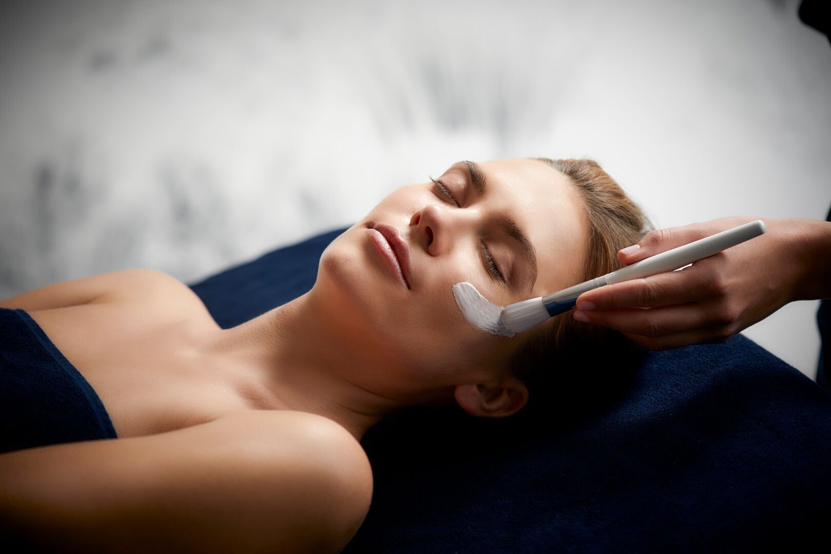 Une femme avec de la crème blanche sur le visage porte son doigt à ses lèvres.