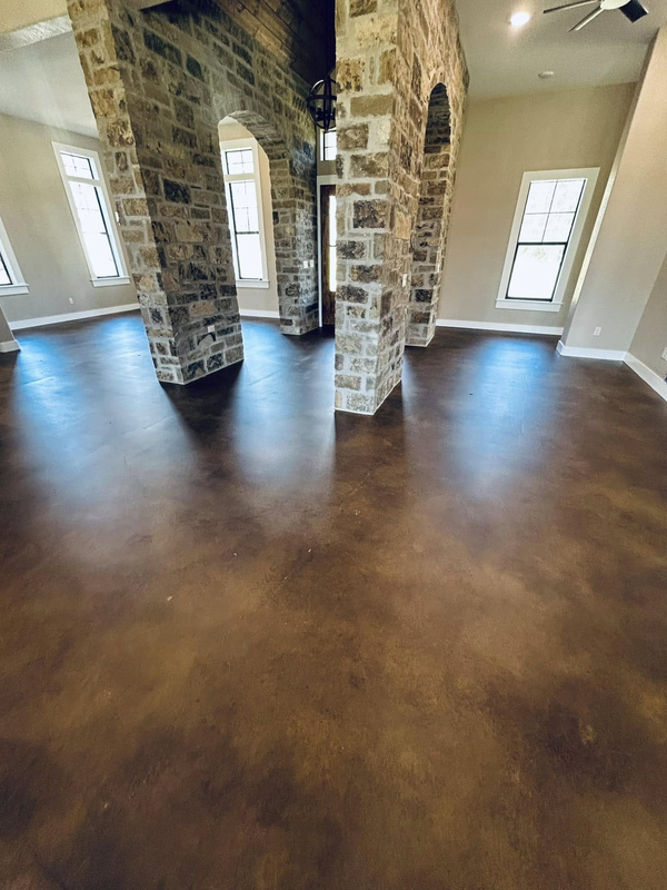 A large, empty room features dark, stained concrete floors and two prominent stone pillars with arched openings.