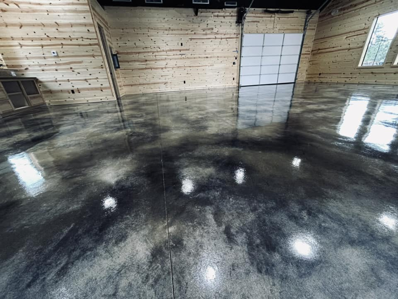 A room with wooden walls and a glossy, dark grey marble-patterned concrete floor reflecting the interior lighting.