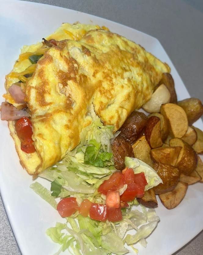 An omelet with diced tomatoes and ham, served with a side of roasted potato wedges and shredded lettuce on a white plate.