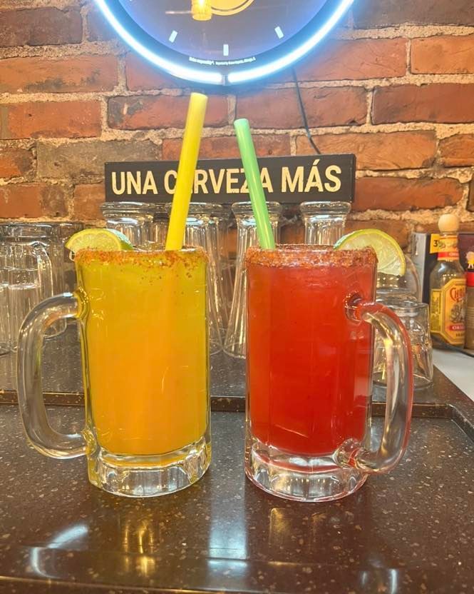 Two glass mugs filled with yellow and red cocktails, garnished with lime wedges and salt rims, on a bar counter.