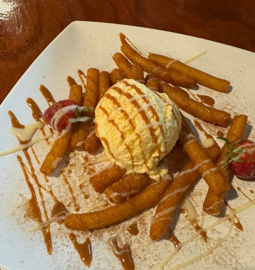 Churros served with a scoop of vanilla ice cream, caramel drizzle, and fresh strawberries on a square white plate.