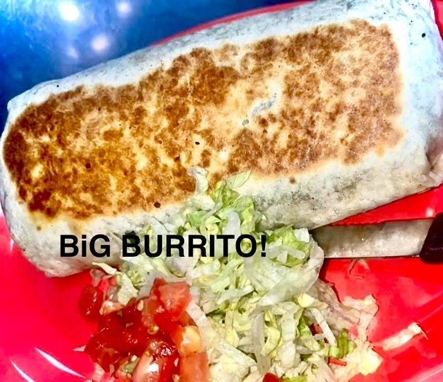 A large, golden-brown grilled burrito sits on a red plate next to a fresh salad of shredded lettuce and chopped tomatoes.