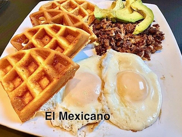 A plate featuring golden waffles, two sunny-side-up eggs, a serving of shredded meat, and sliced avocado.