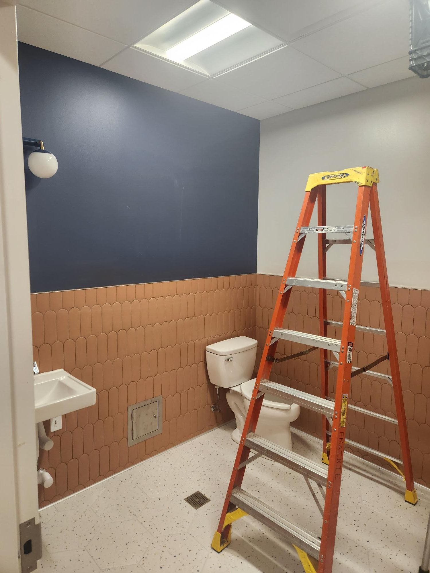A bathroom with a toilet , sink and ladder.