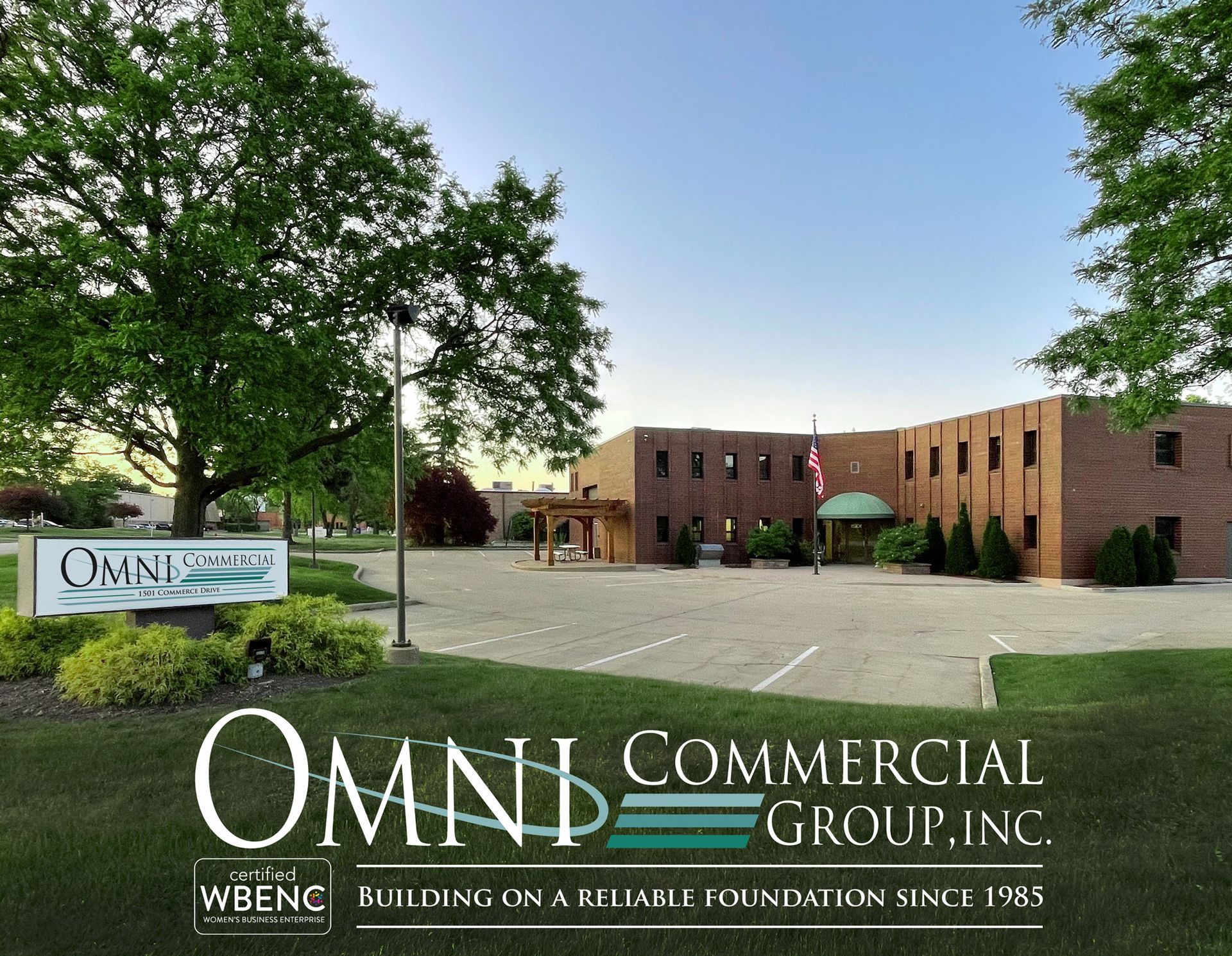 Omni Commercial Group building with sign, trees, and flag on a sunny day.