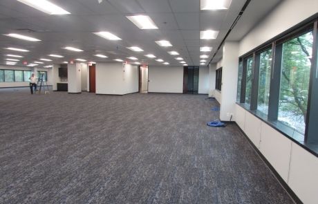 A large empty room with a carpeted floor and lots of windows