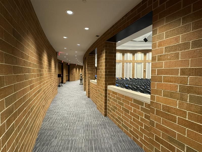 A long hallway with brick walls and a window leading to an auditorium - Elgin, IL - Omni Commercial Group, Inc