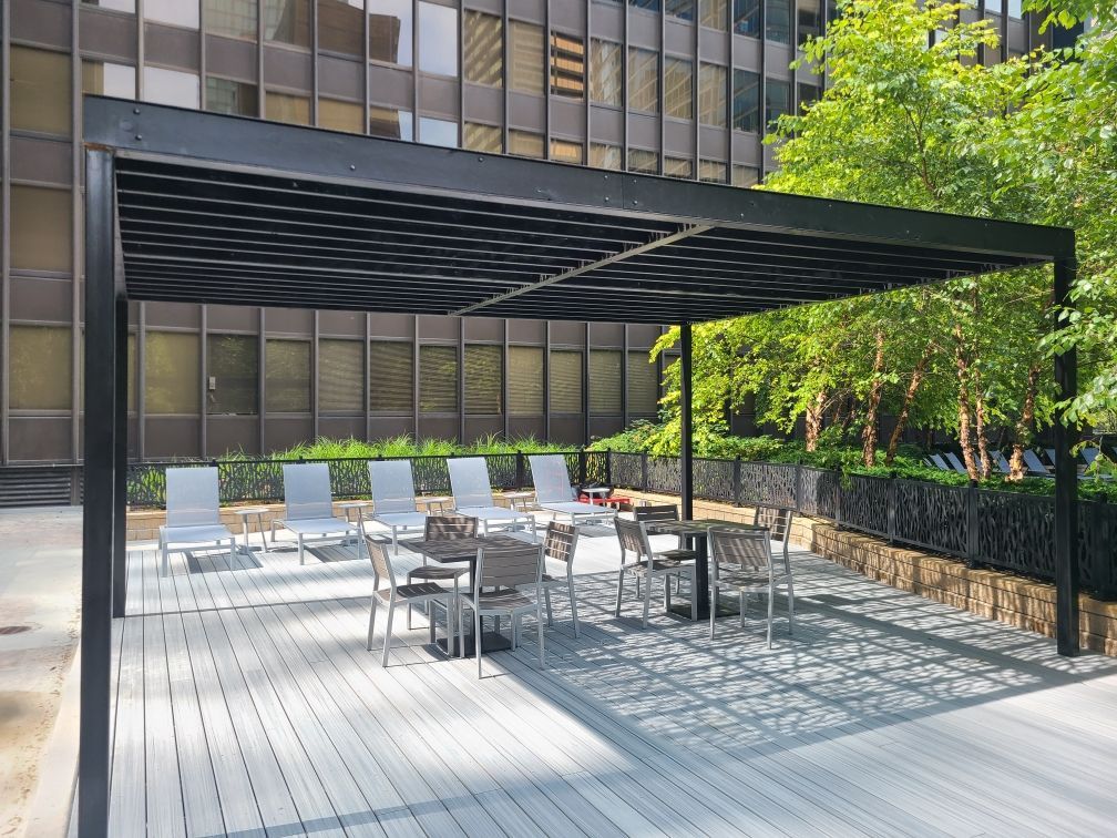 A deck with tables and chairs under a pergola in front of a building.