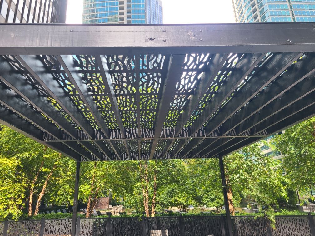 A pergola in a park with trees and a building in the background.