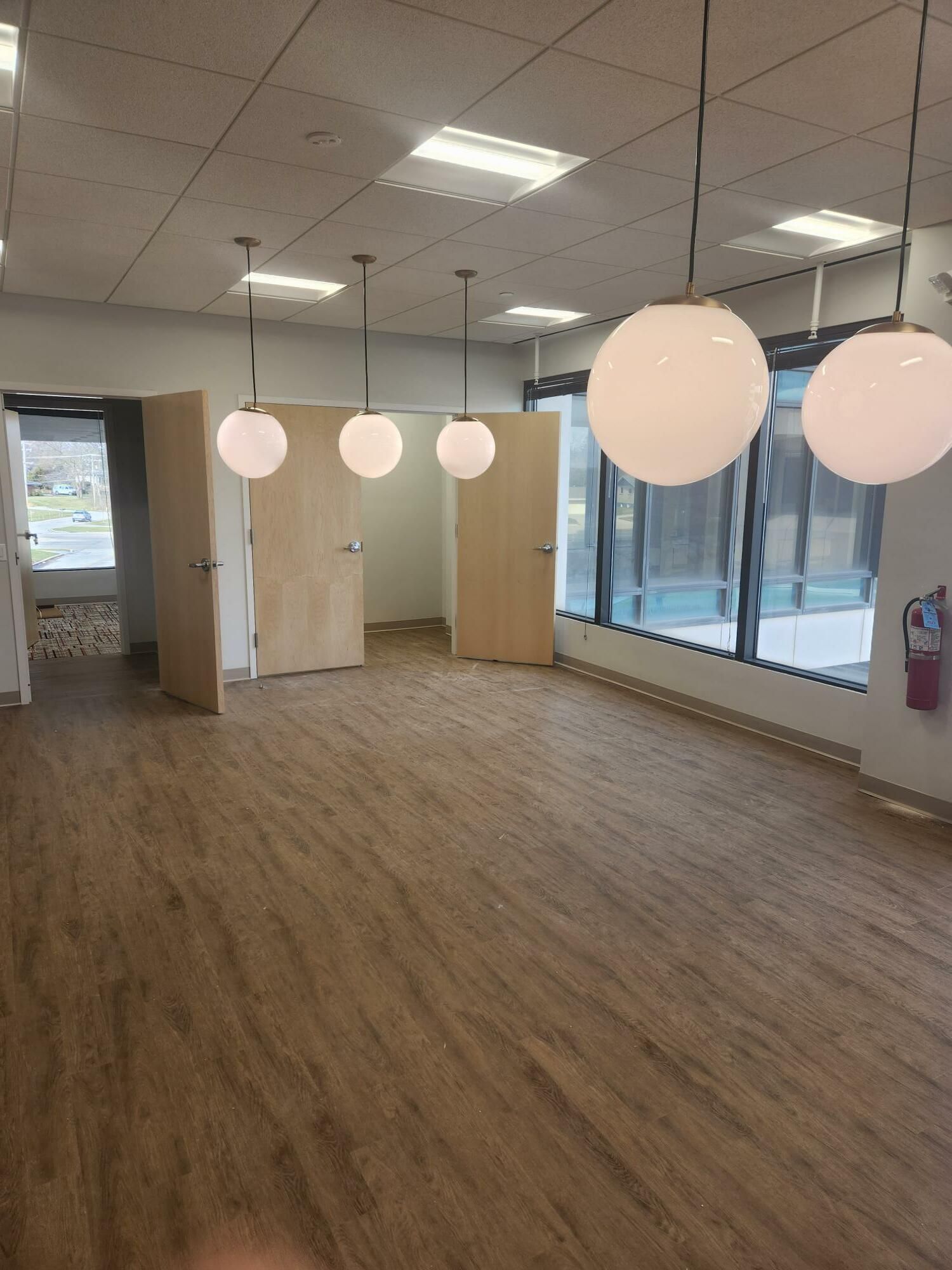 A large empty room with wooden floors and ceiling lights hanging from the ceiling.