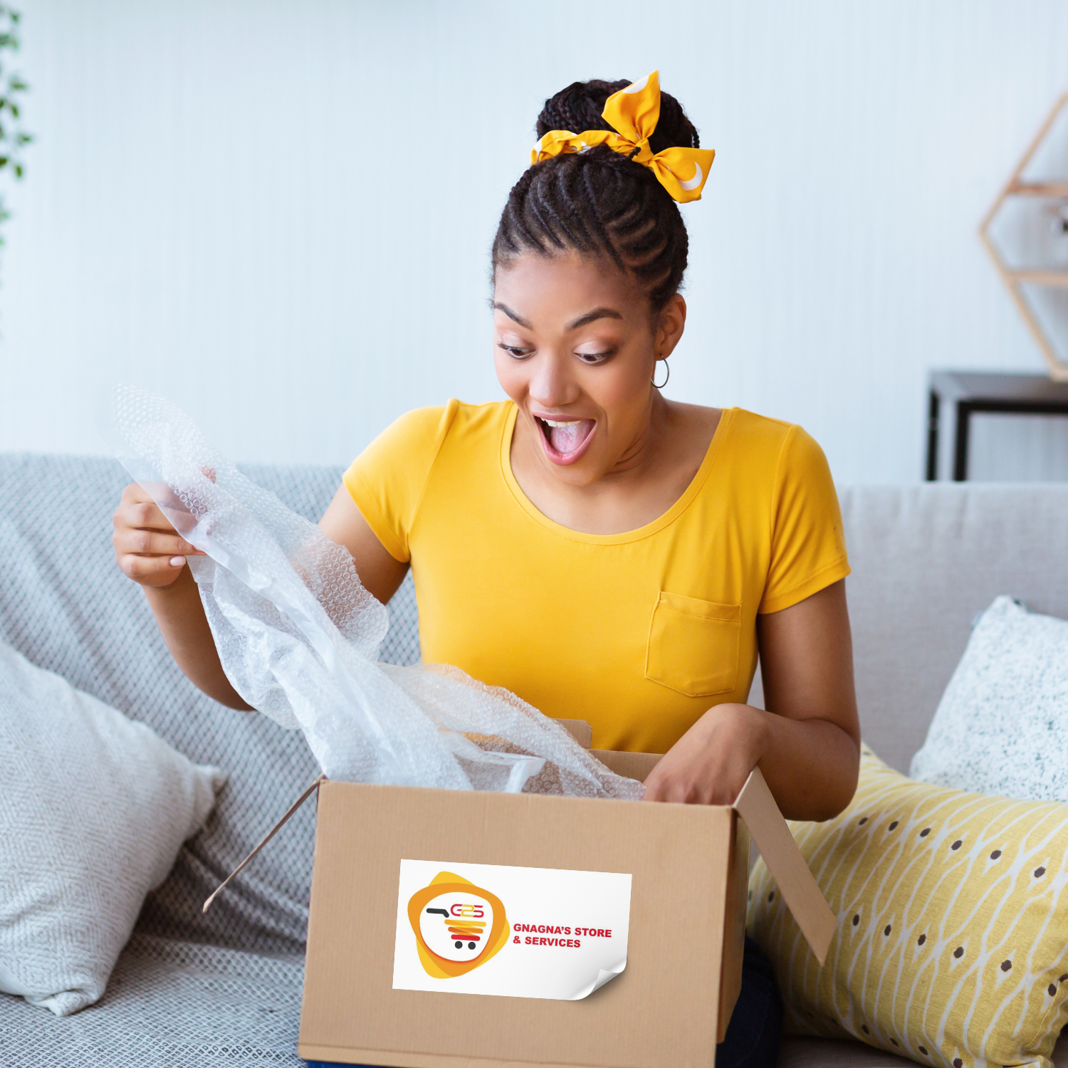 Une femme en chemise jaune est assise sur un canapé et ouvre une boîte en carton.