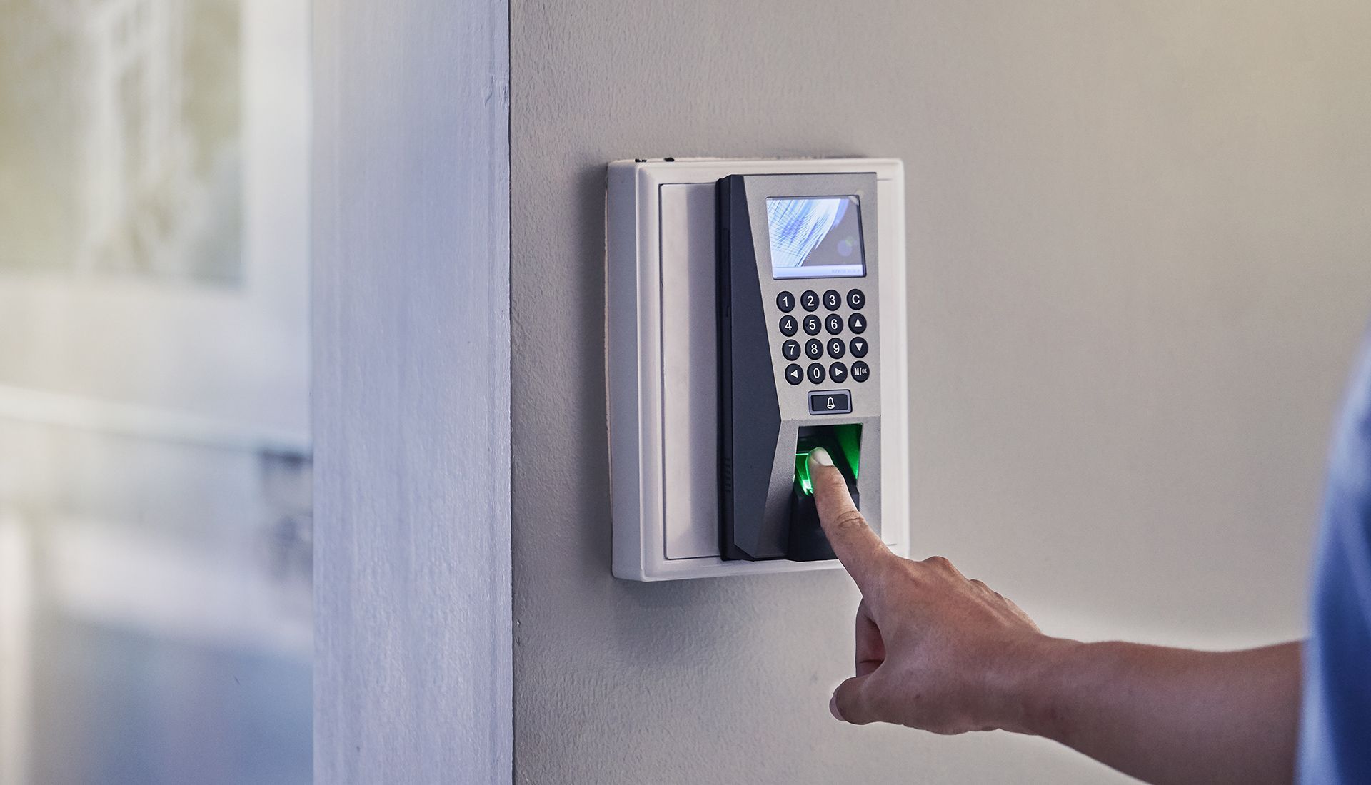 Finger pressed on a fingerprint scanner, mounted on a wall.