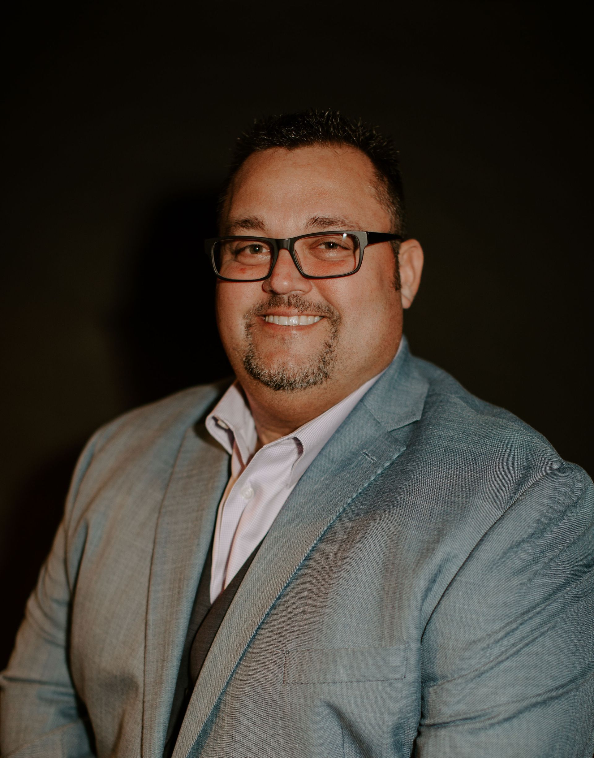 A man in a suit and glasses is smiling for the camera.