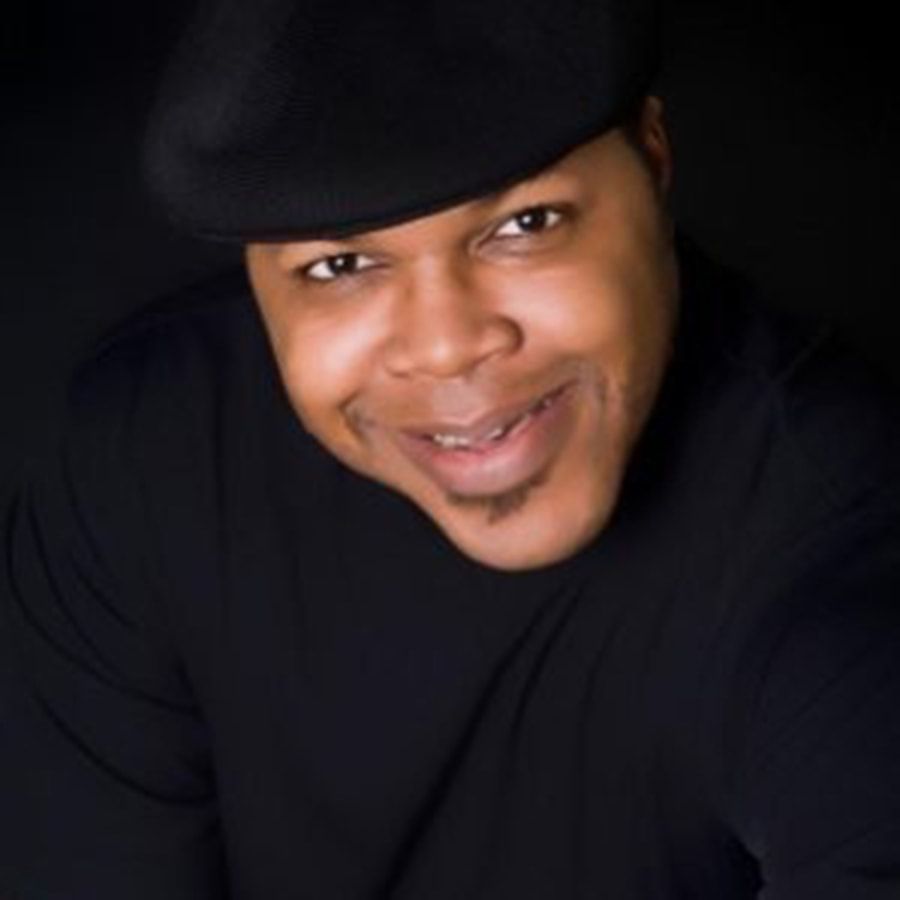 A man wearing a hat and a black shirt smiles for the camera