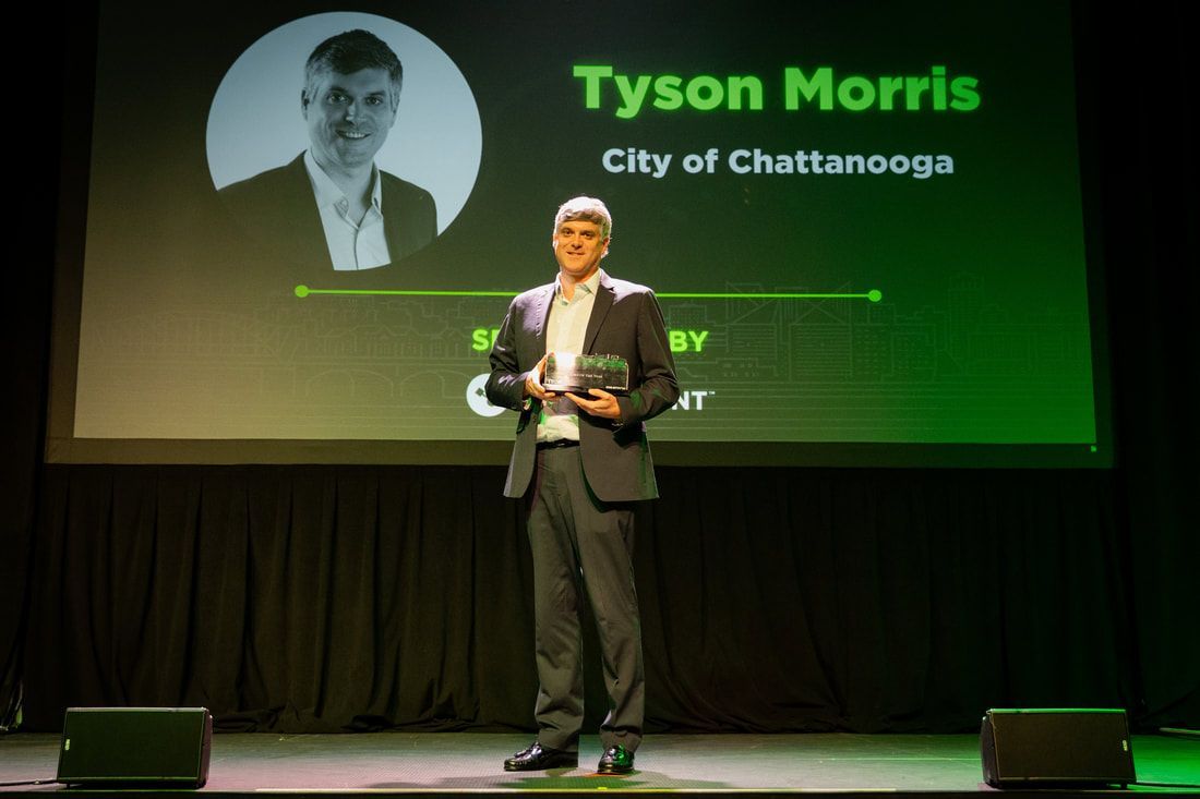A man in a suit is standing on a stage in front of a large screen with the name tyson morris on it.