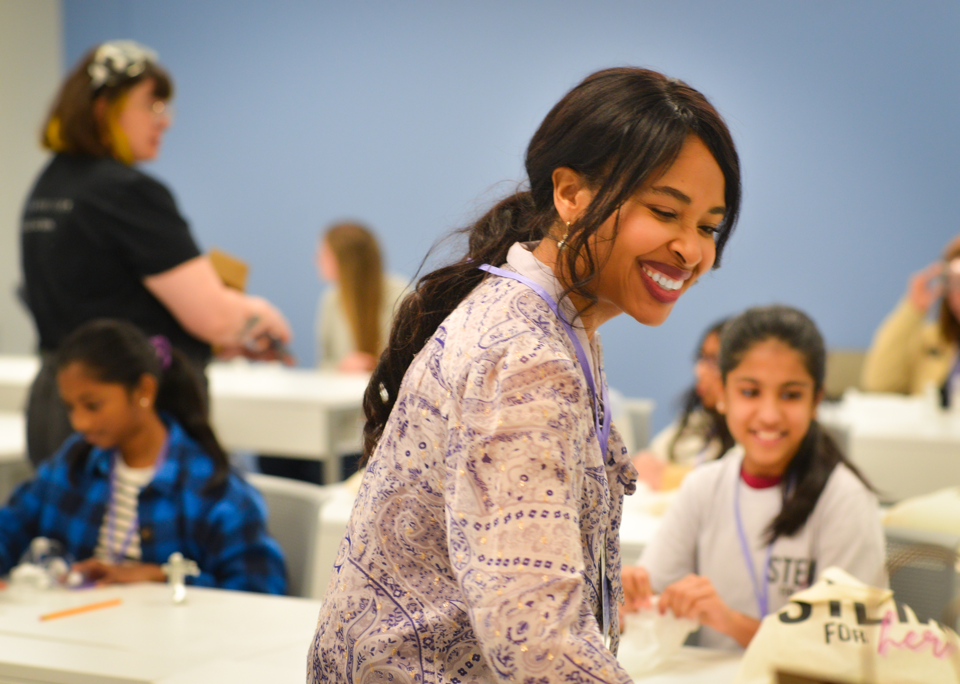 A woman is smiling in front of a group of children in a classroom.