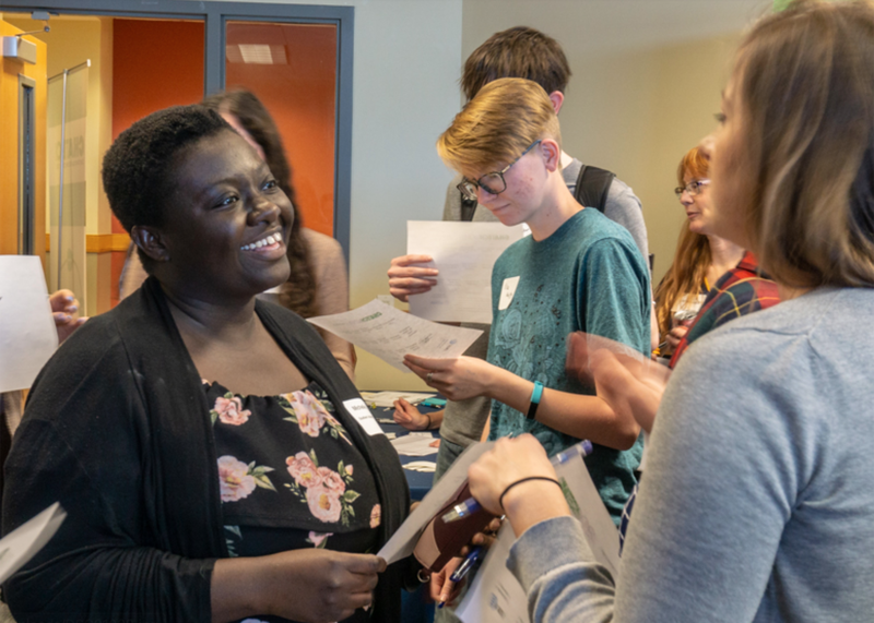A group of people are standing around a table talking to each other.