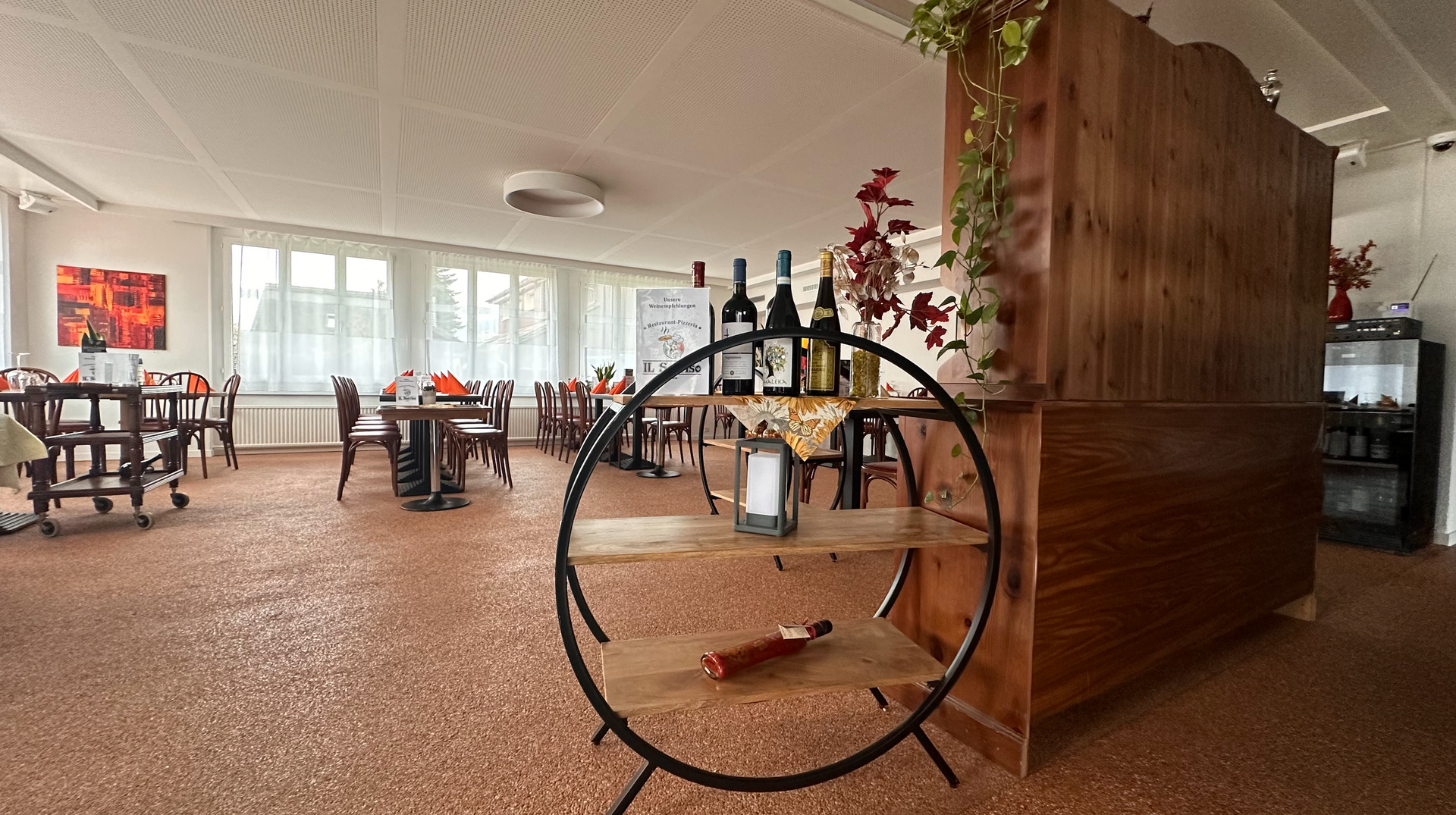 Une grande pièce avec des tables et des chaises et une étagère avec des bouteilles de vin dessus.