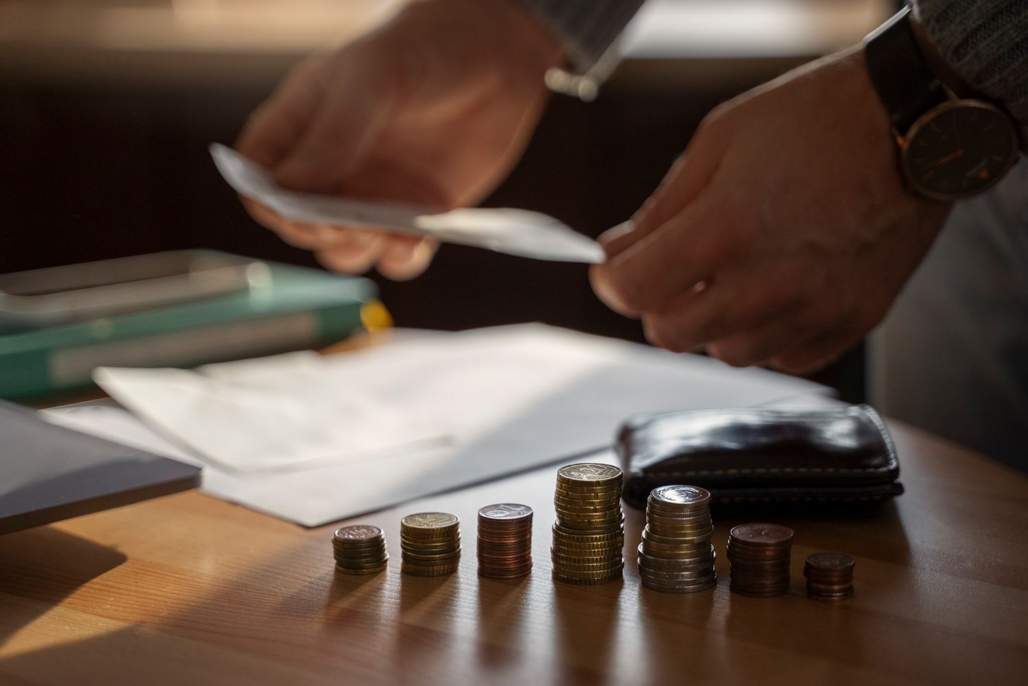 Person sorting papers, counting coins on a table with a wallet and other items, focused on finances.