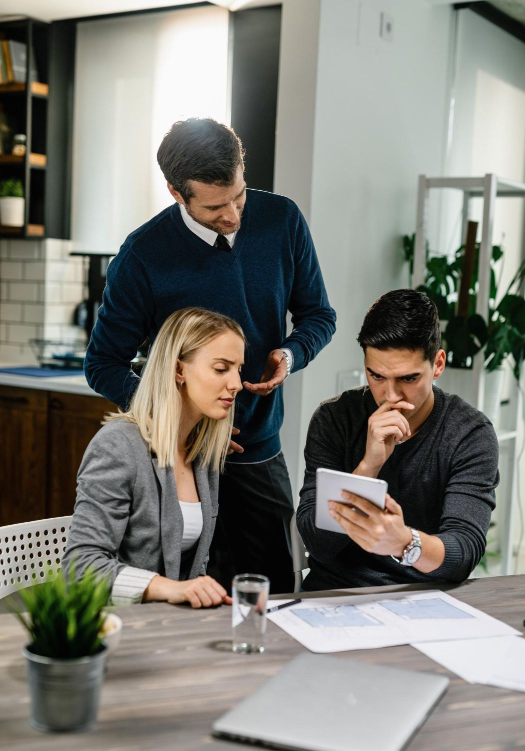 Three people reviewing a tablet together at a table. One man looks at tablet, the other two observe.