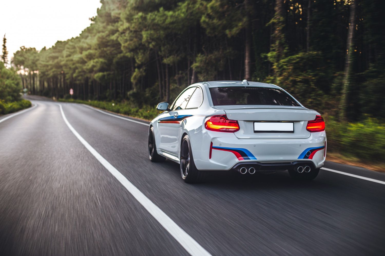 Blue car driving along a coastal road lined with palm trees under a bright blue sky.