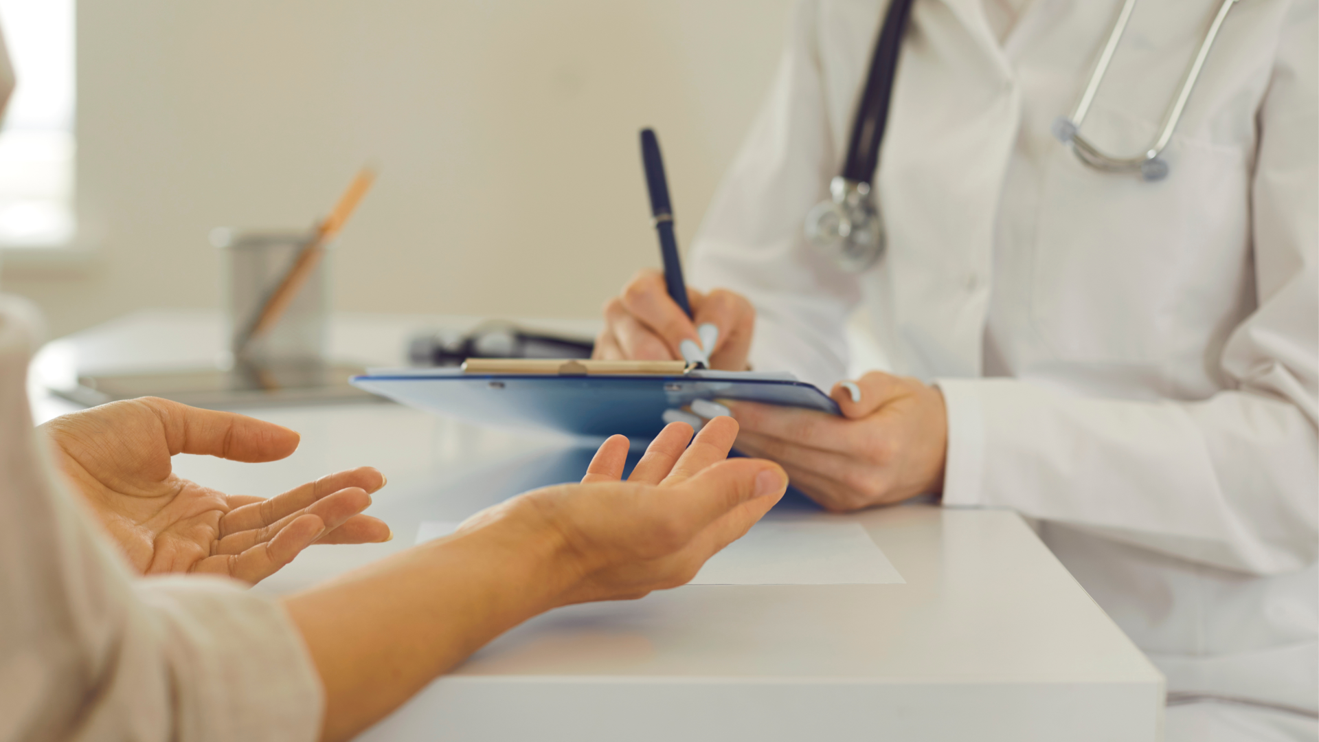 Woman packing a cardboard box, smiling. Boxes and another person nearby, in a room, light setting.