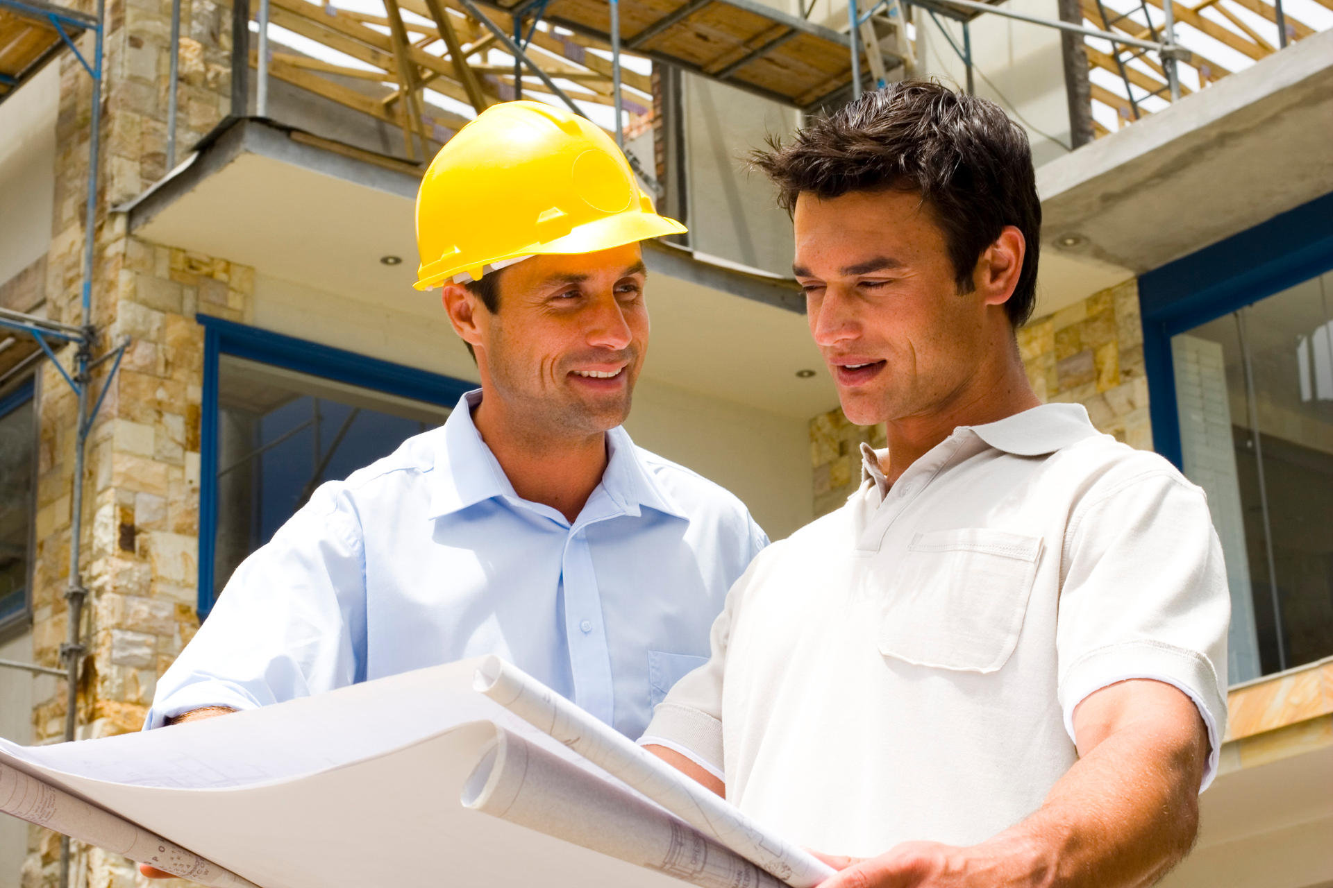 Two-story light green house with a white balcony and roof, on a gravel driveway under a clear blue sky.
