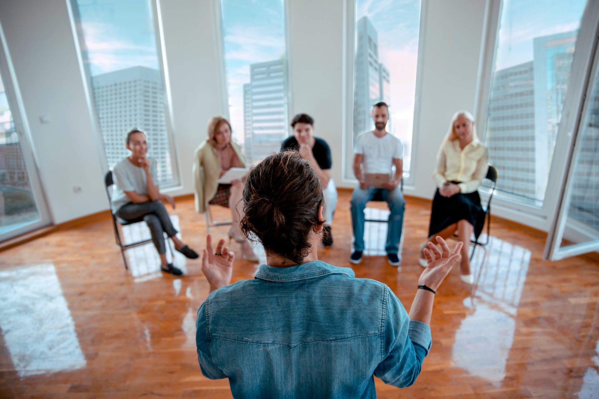Woman packing a cardboard box, smiling. Boxes and another person nearby, in a room, light setting.