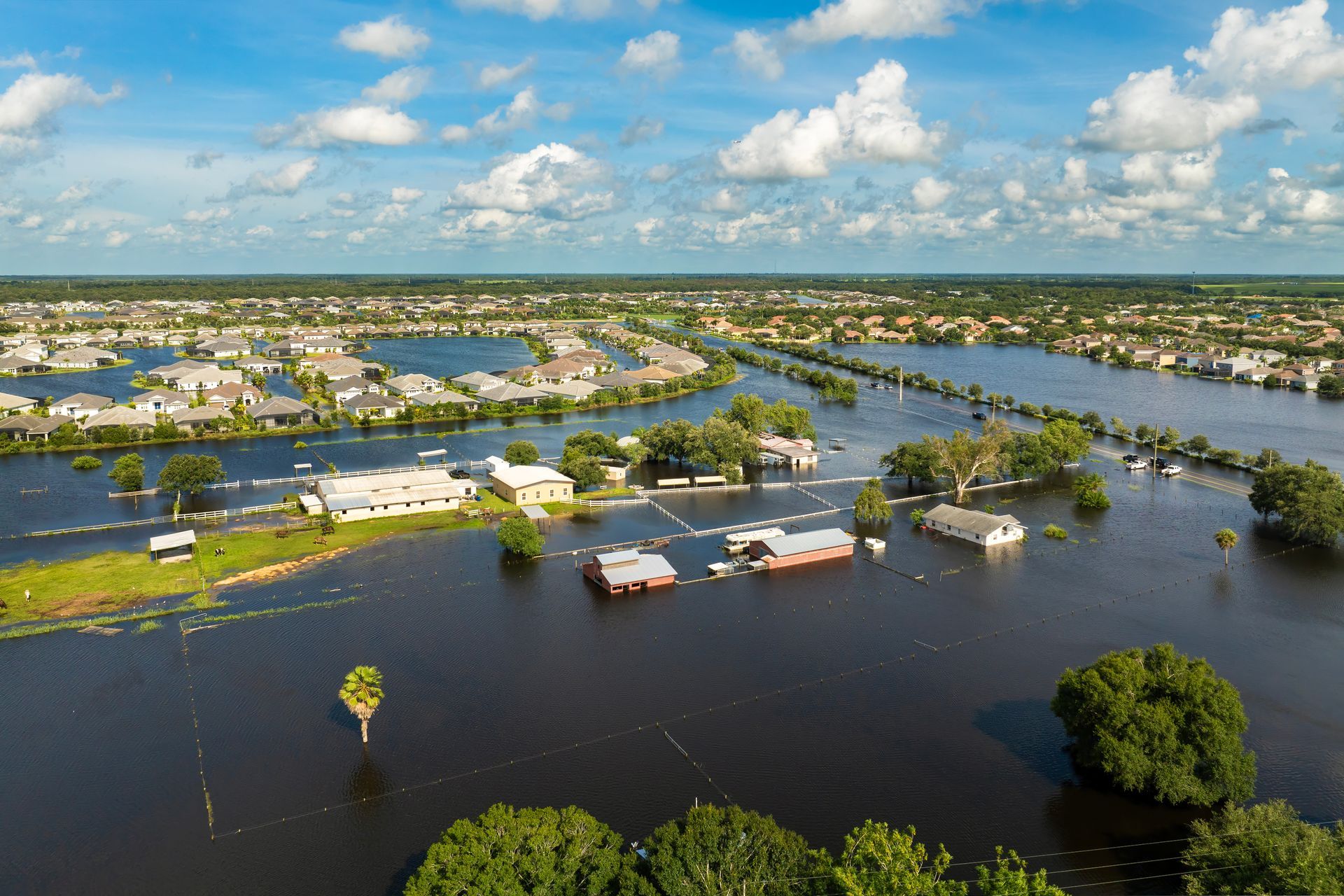 Flooded suburban homes after a disaster, under a cloudy sky.